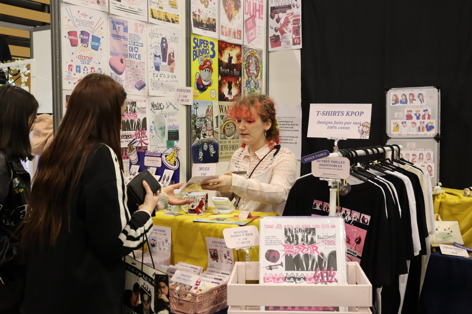Photo de l'artiste sur son stand en convention, parlant avec une cliente